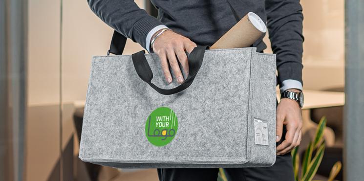 Ein Mann im Business-Outfit hat eine graue Filztasche umhängen. Auf der Tasche ist ein Logo-Aufdruck zu sehen.