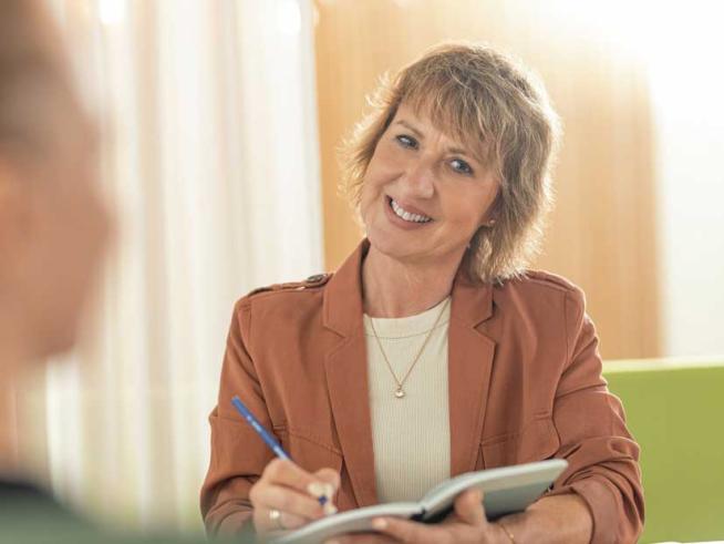 Frau mit Notizbuch in der Hand lächelt freundlich in Kamera