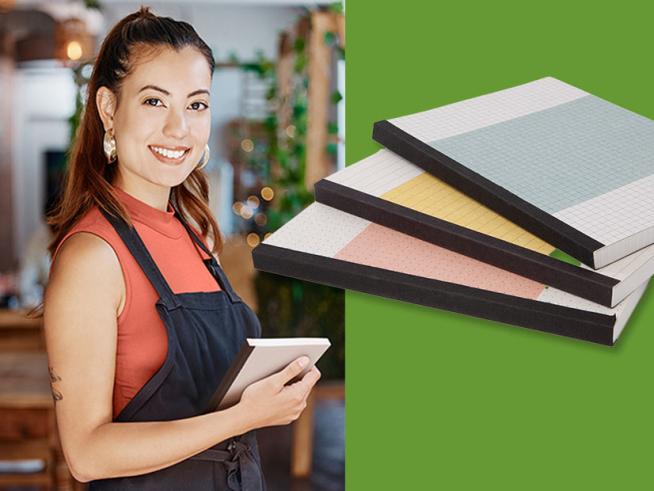 Eine dunkelhaarige Frau mit Schürze im Gastroumfeld hält ein Notizbuch in der Hand