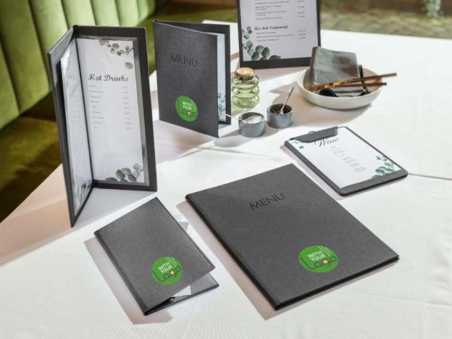 Auf einem Tisch im Restaurant stehen unterschiedliche Speisekartenmappen mit Logoaufdruck